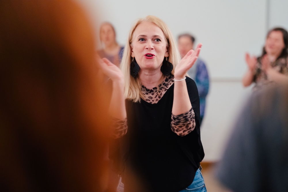 Eine Frau breitet ihre Arme aus. Sie ist schwarz gekleidet und hat helle Haare.